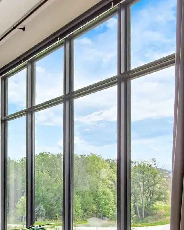 Floor-to-ceiling black-framed windows in a living room looking out on trees
